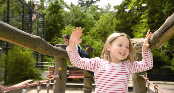 Mädchen spielt auf einem Holzspielplatz. Im Hintergund ein anderes Mädchen.