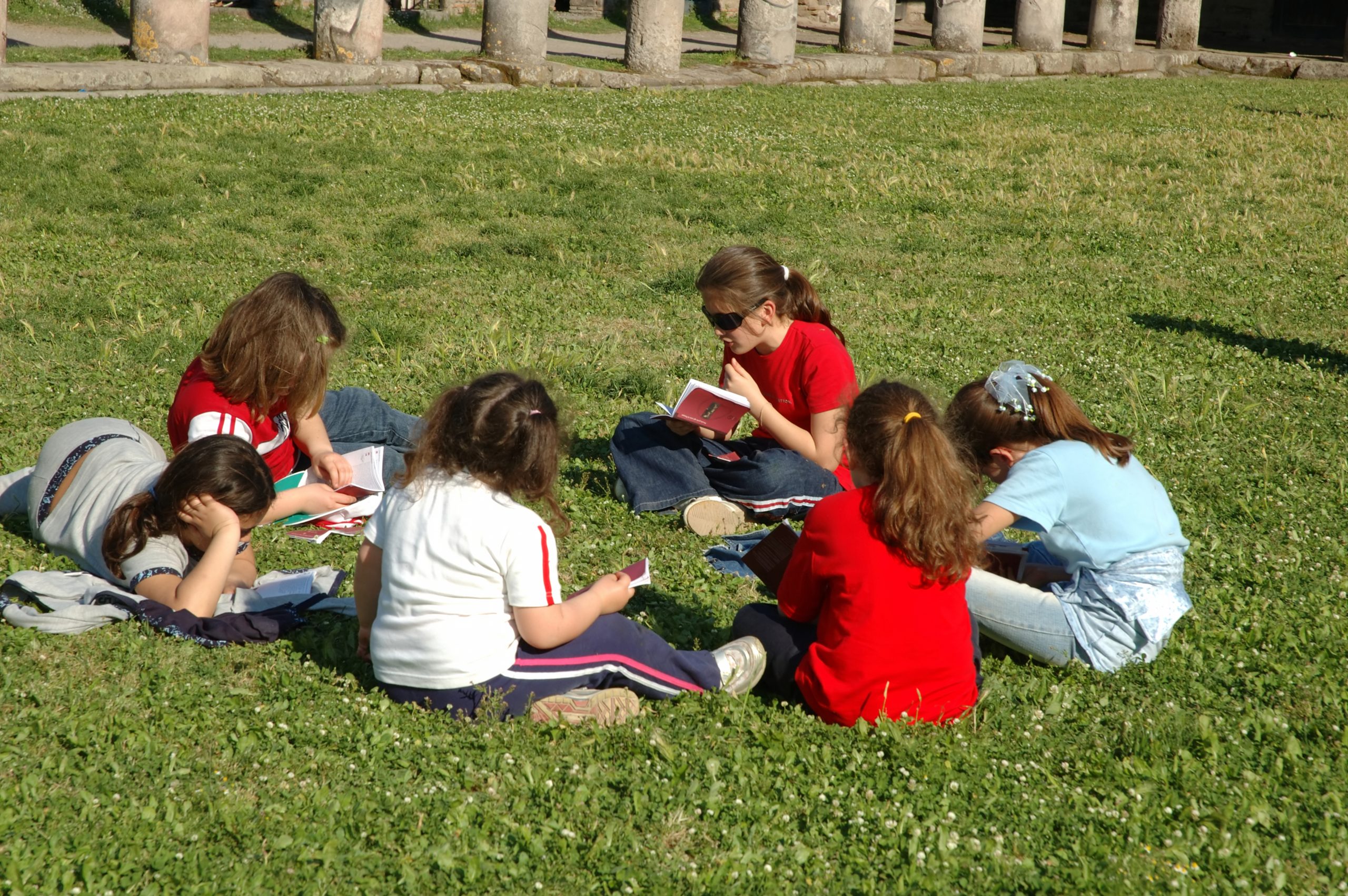 Kinder sitzen auf einer Wiese im Kreis und lesen