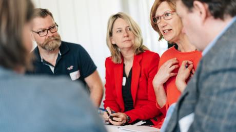 Mehrere Personen sitzen im Halbkreis an einem Tisch und sprechen miteinander.