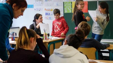 Abgebildet ist ein Klassenzimmer, in dem mehrere Schüler*innen und eine Lehrerin miteinander lernen und sprechen.